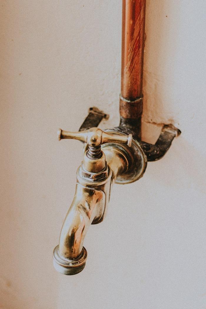A copper pipe feeding a brass tap on a white wall.