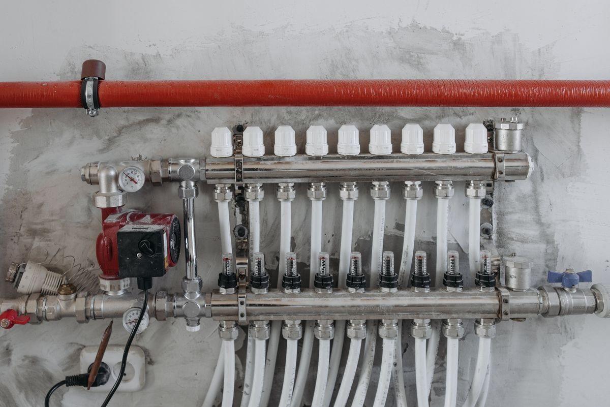 An underfloor heating manifold with pump and pipe connections on a wall.