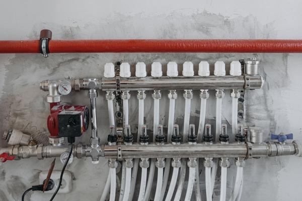 An underfloor heating manifold with pump and pipe connections on a wall.