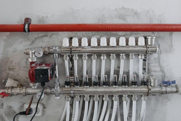 An underfloor heating manifold with pump and pipe connections on a wall.