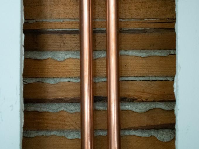 Two copper pipes running vertically through a chased-out wall.