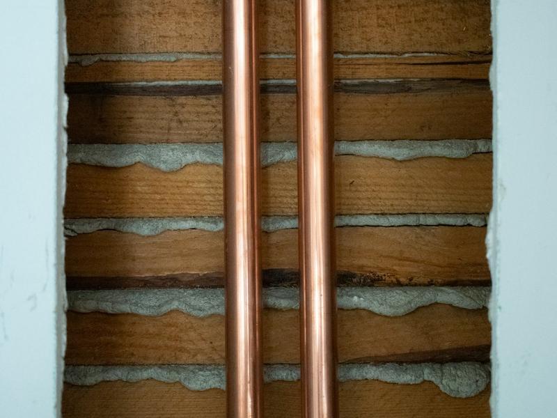 Two copper pipes running vertically through a chased-out wall.