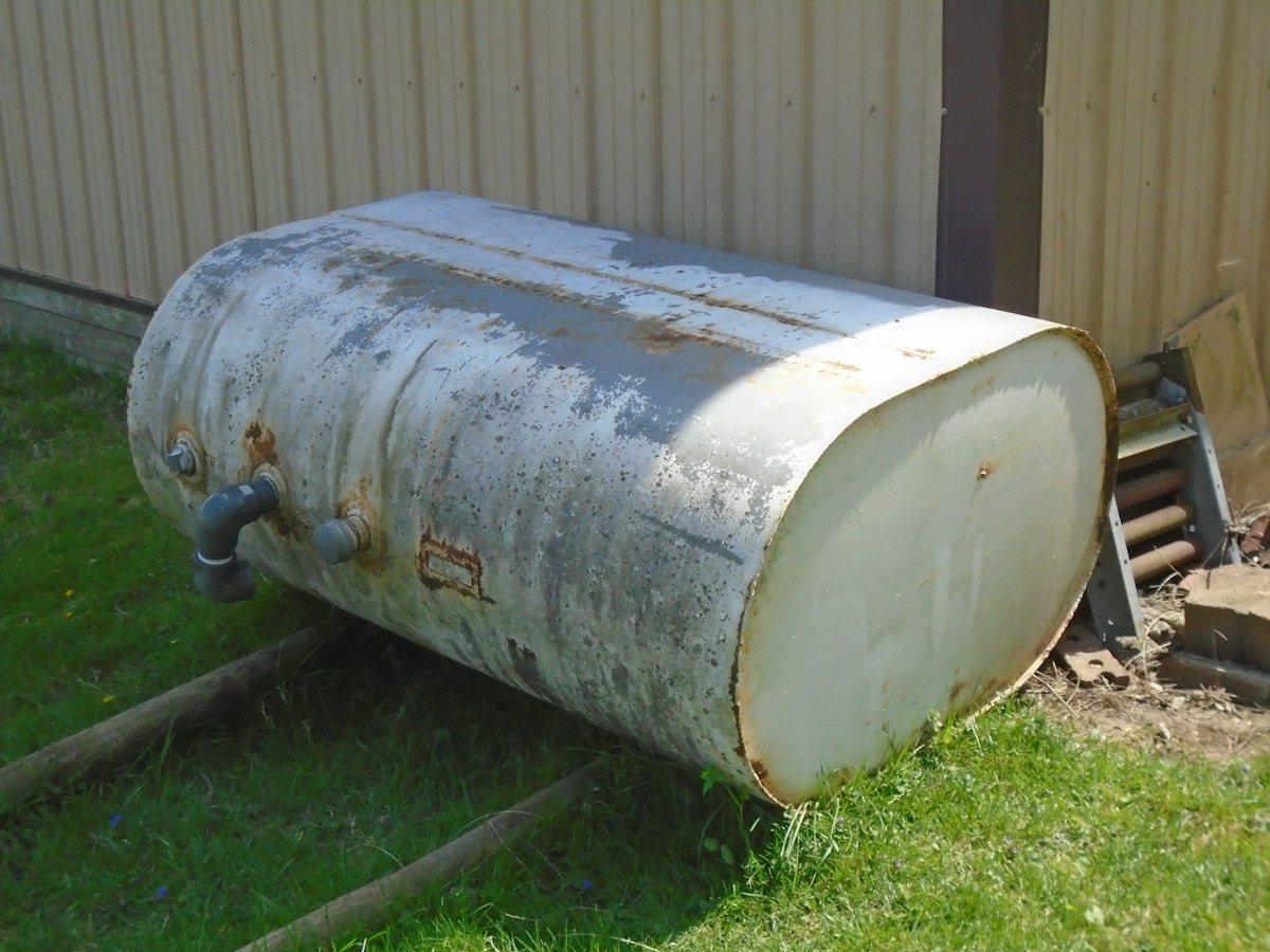A weathered steel heating oil tank on the grass beside a house.