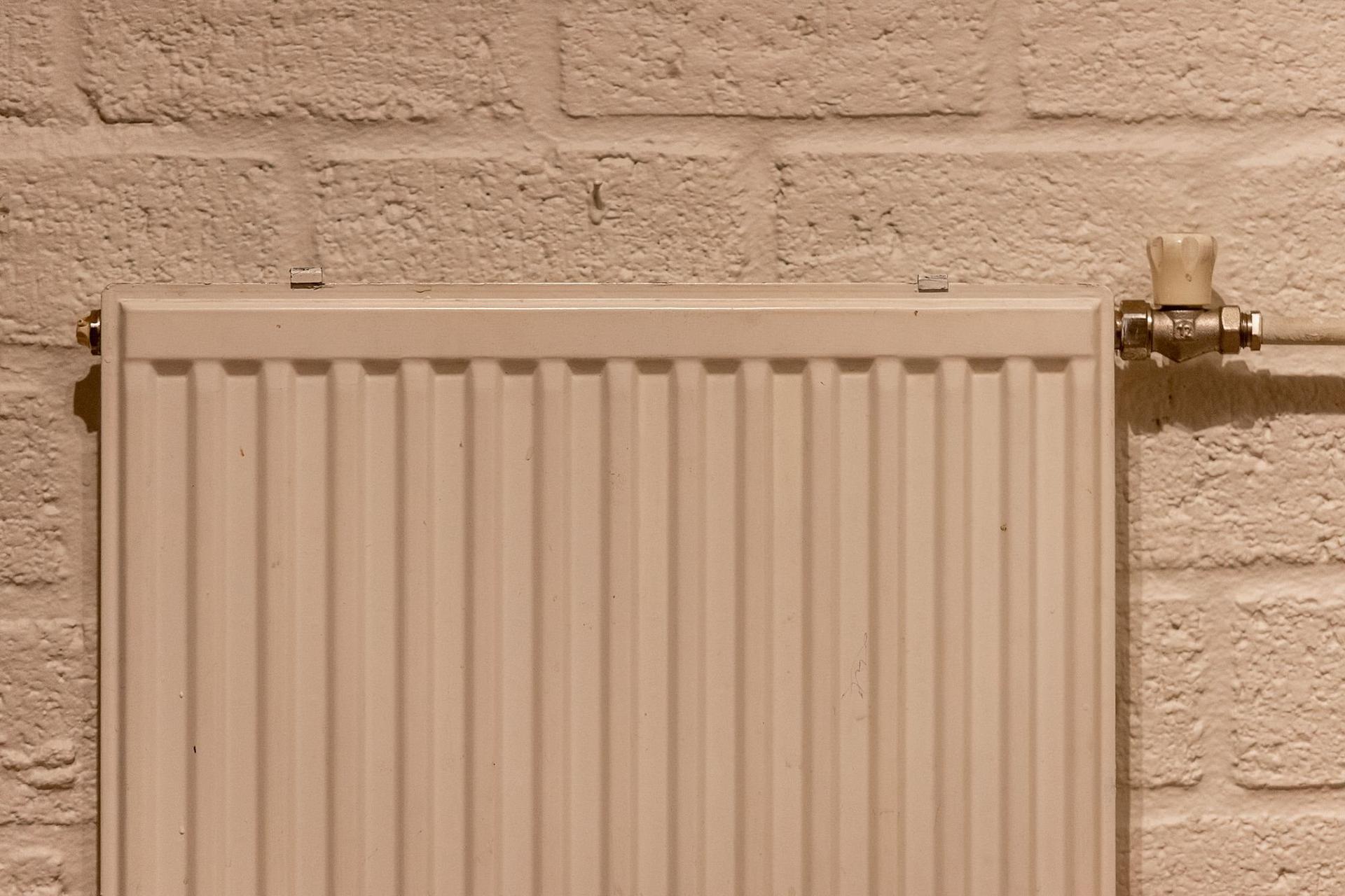 A white panel radiator and its valve mounted on a painted brick wall.