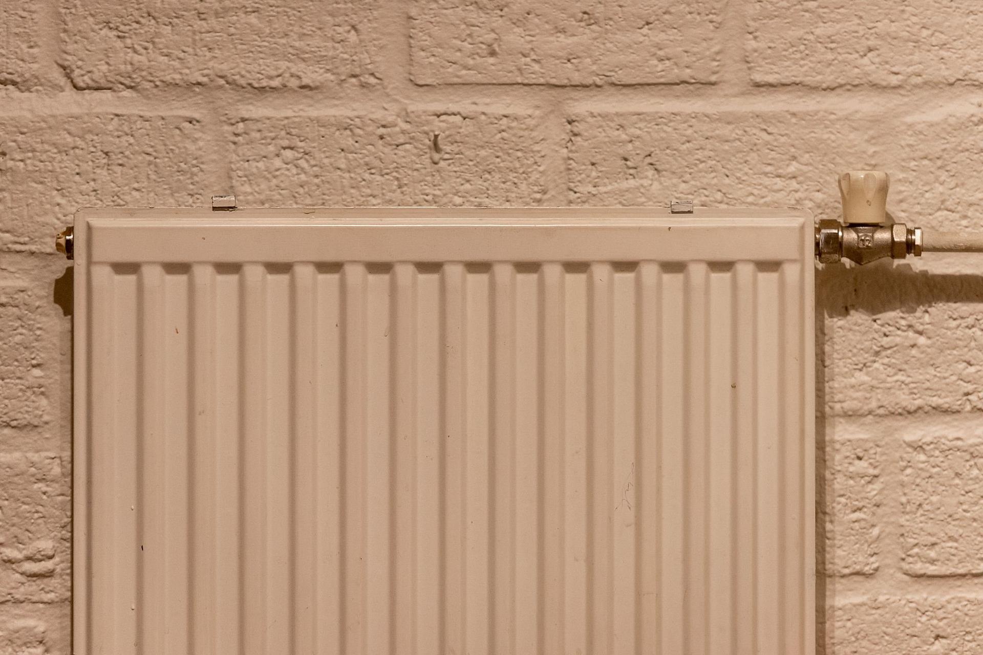 A white panel radiator and its valve mounted on a painted brick wall.