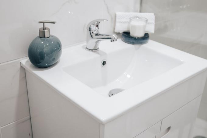 A white ceramic basin on a white vanity unit with a chrome mixer tap and a blue soap dispenser.