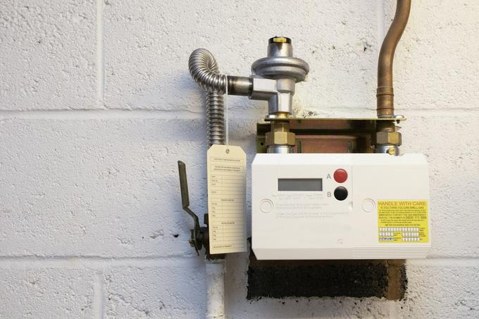 A domestic gas meter and regulator mounted on a painted block wall.