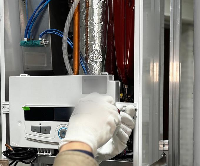 Close-up of gloved hands adjusting the control panel inside an open wall-mounted boiler.