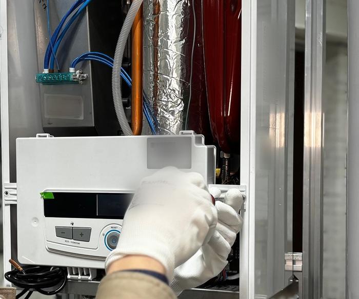 Close-up of gloved hands adjusting the control panel inside an open wall-mounted boiler.
