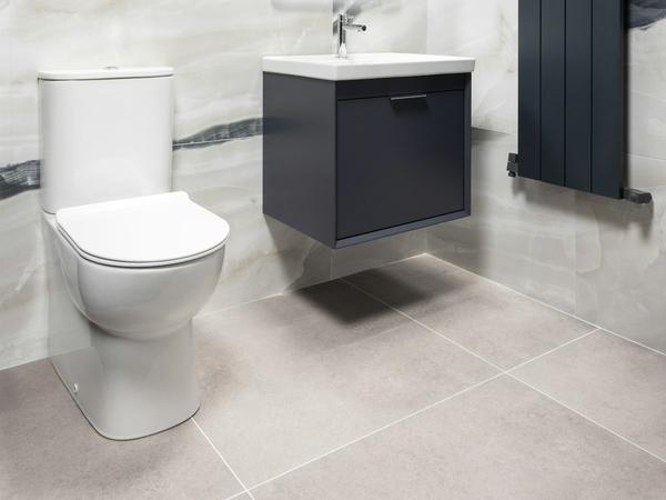 A white close-coupled toilet beside a dark grey wall-hung vanity unit and a vertical radiator in a marble-tiled bathroom.
