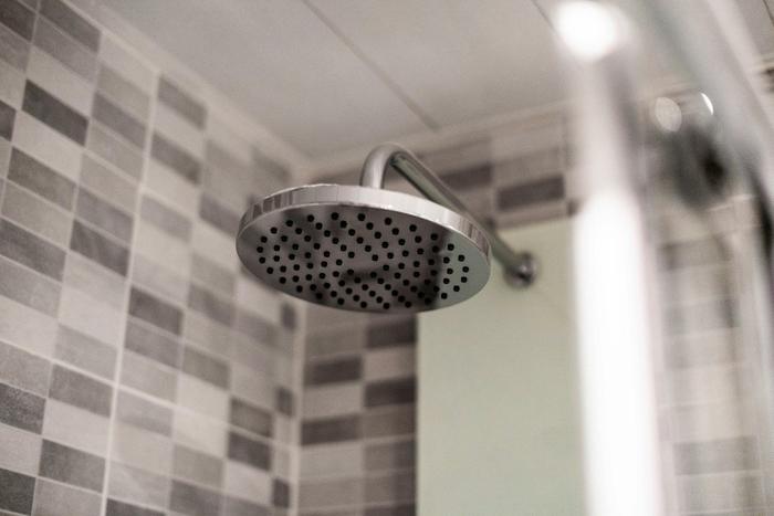 A chrome rainfall shower head against grey tiles.
