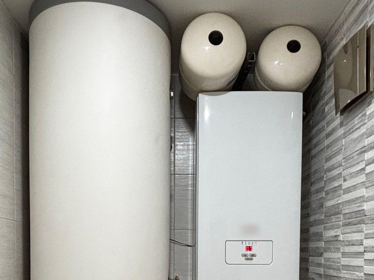 A wall-hung boiler with expansion vessels installed next to a tall hot water cylinder.