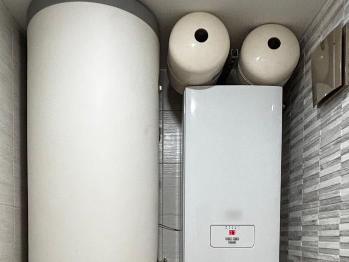 A wall-hung boiler with expansion vessels installed next to a tall hot water cylinder.