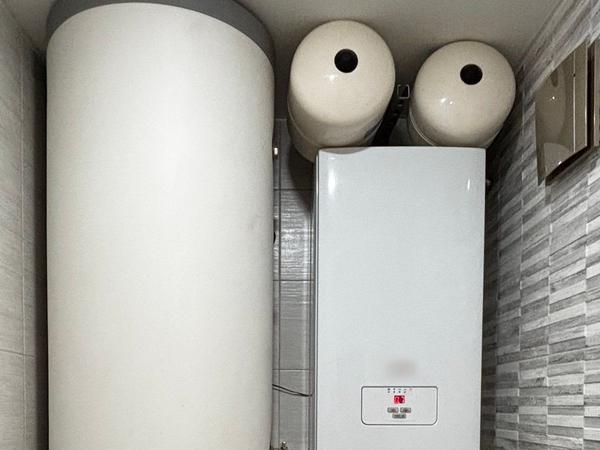 A wall-hung boiler with expansion vessels installed next to a tall hot water cylinder.