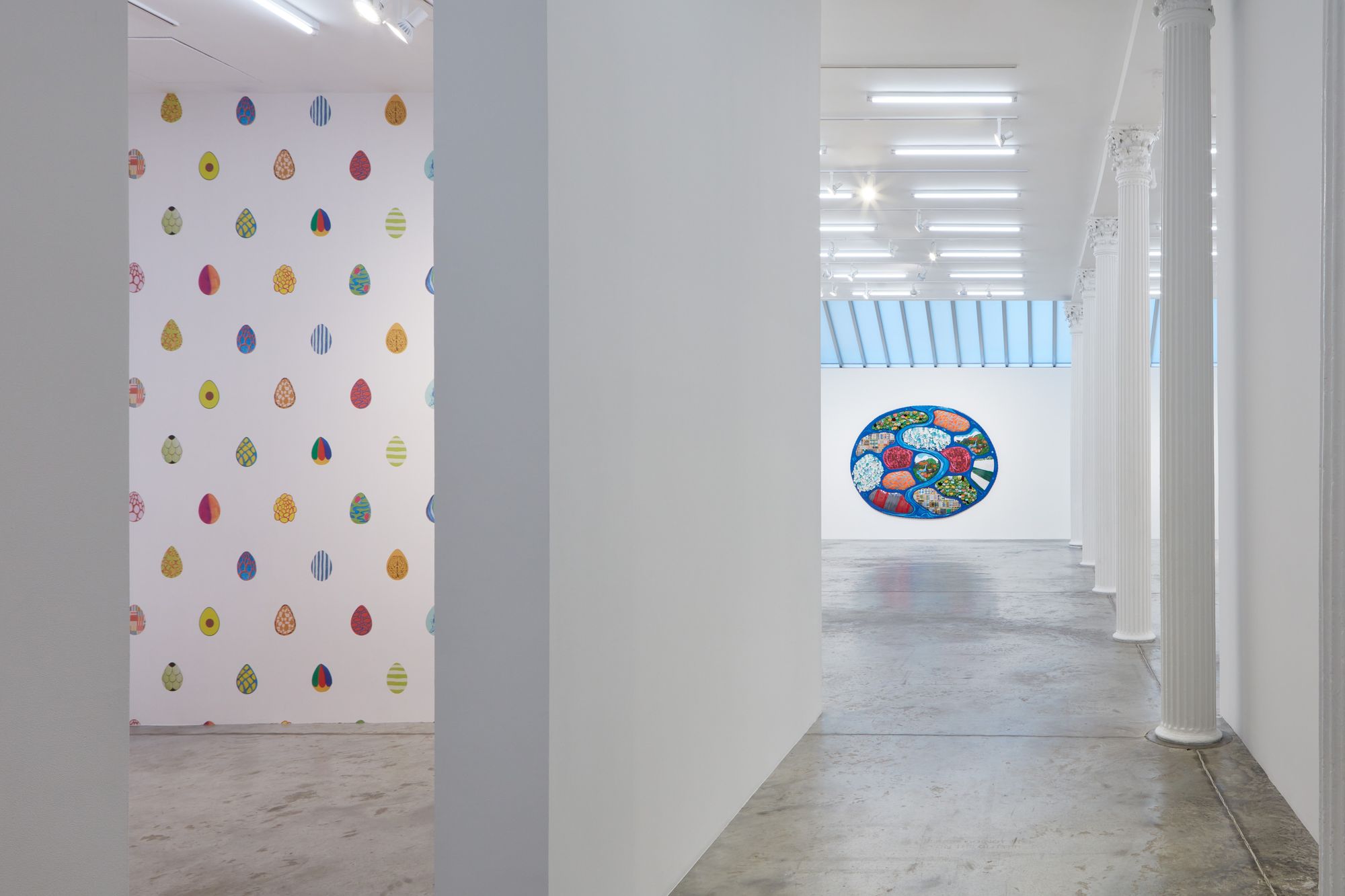 Installation view in white walled room with earth like sculpture in background and spotted wallpaper in foreground