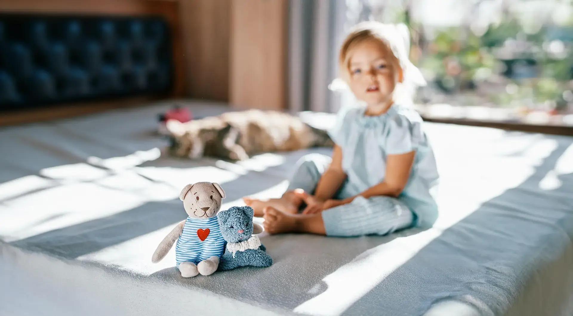Дете стои на легло до плюшени играчки