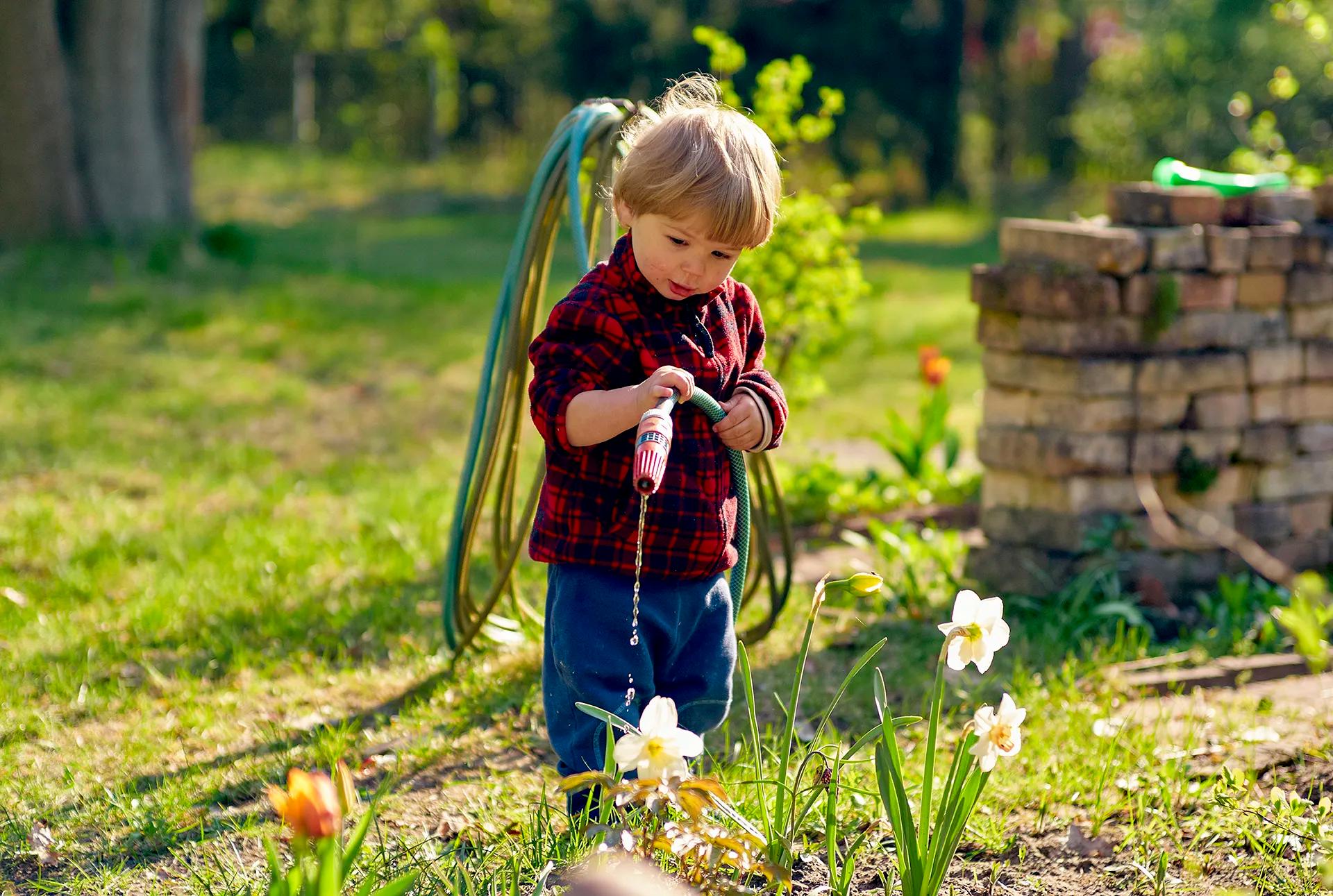 малко дете полива цветя в градината с маркуч пролетни монтесори занимания навън