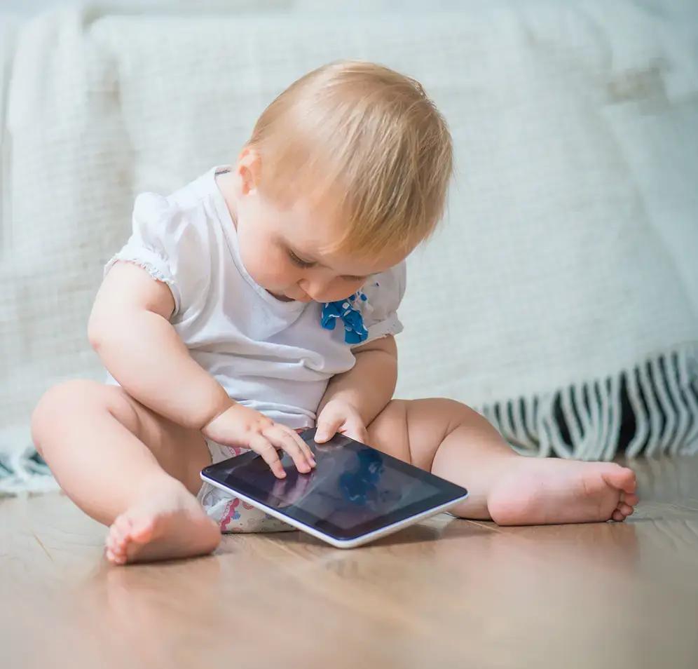 Малко дете гледа таблет, седнало на земята