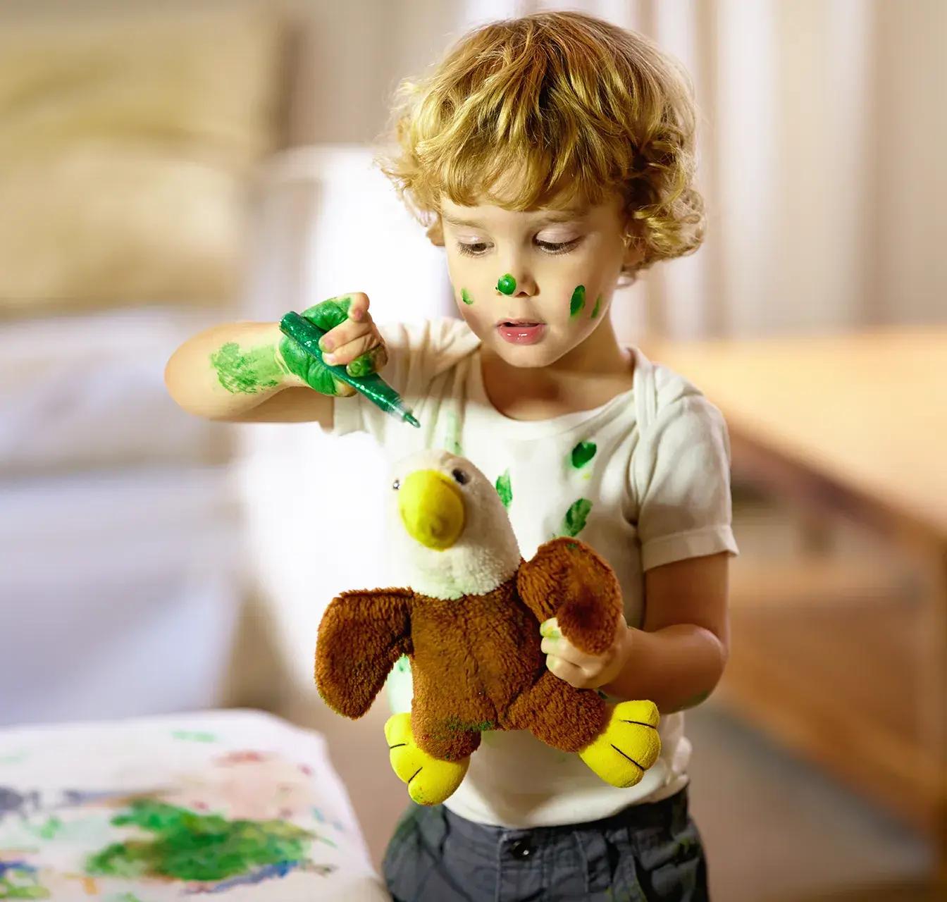 Момче със зелена боя се забавлява, като боядисва и лицето си.