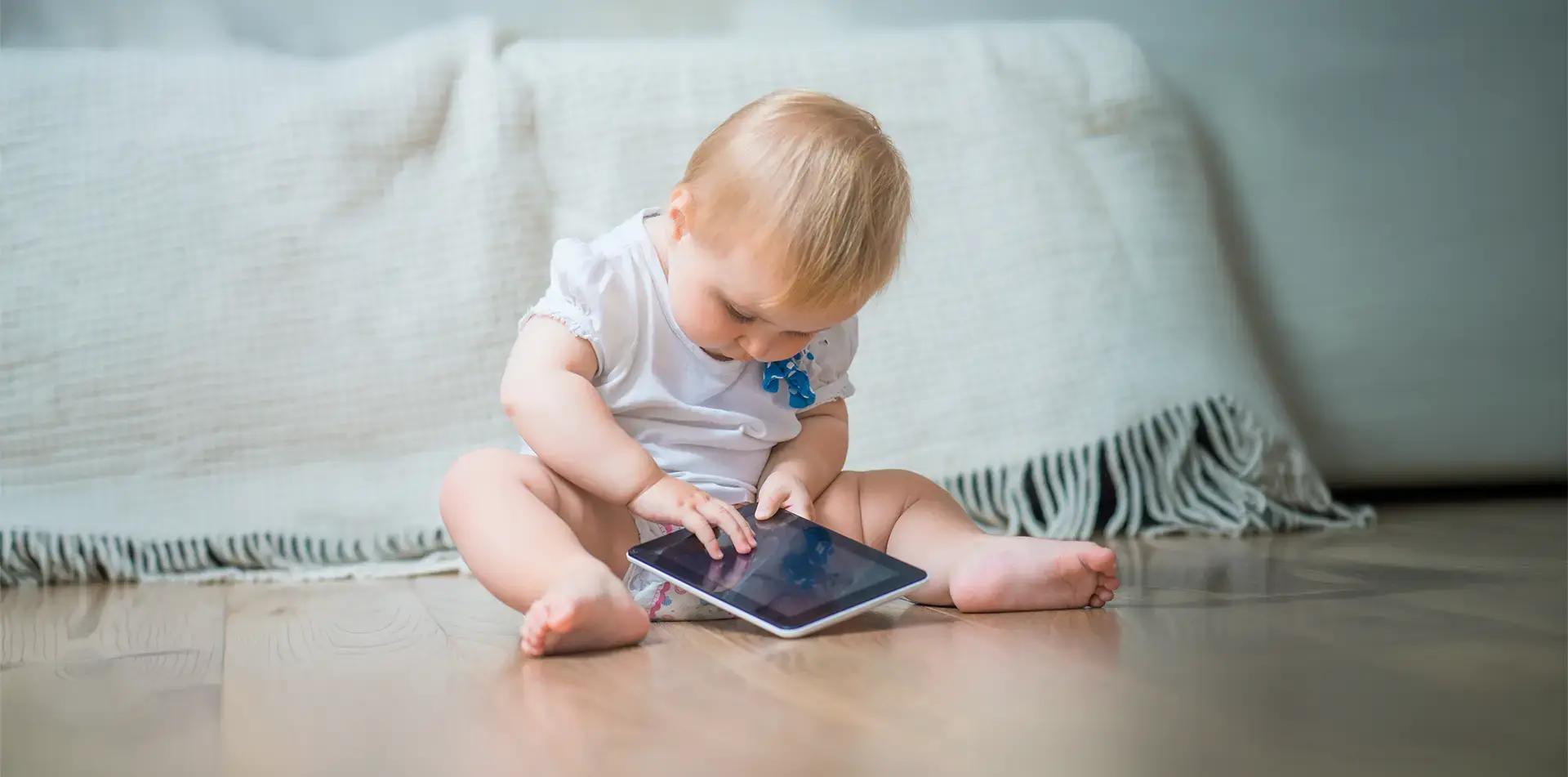 Малко дете гледа таблет, седнало на земята