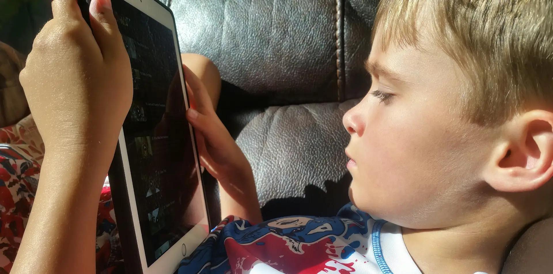 Малко дете гледа таблет, седнало на диван