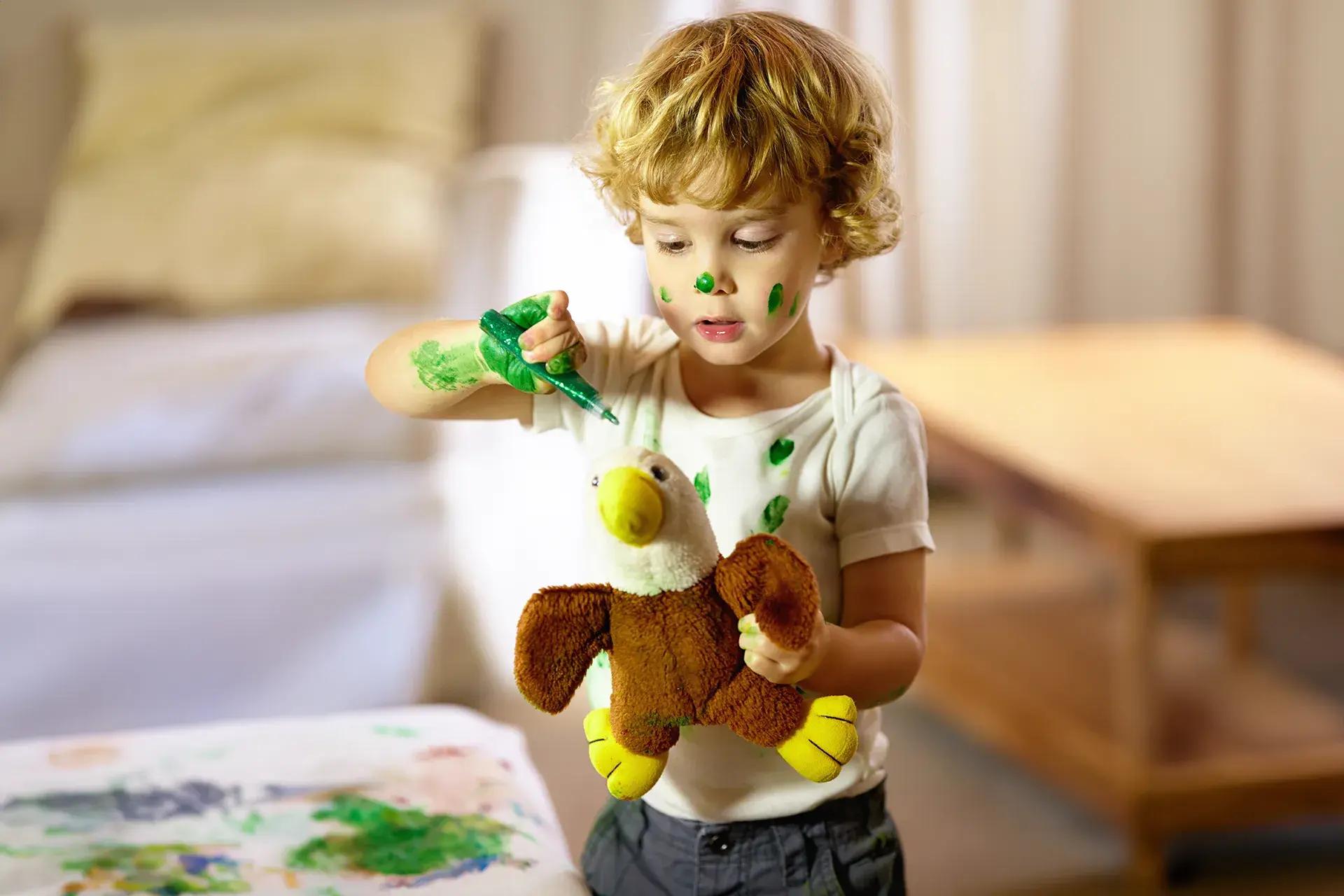 Момче със зелена боя се забавлява, като боядисва и лицето си.