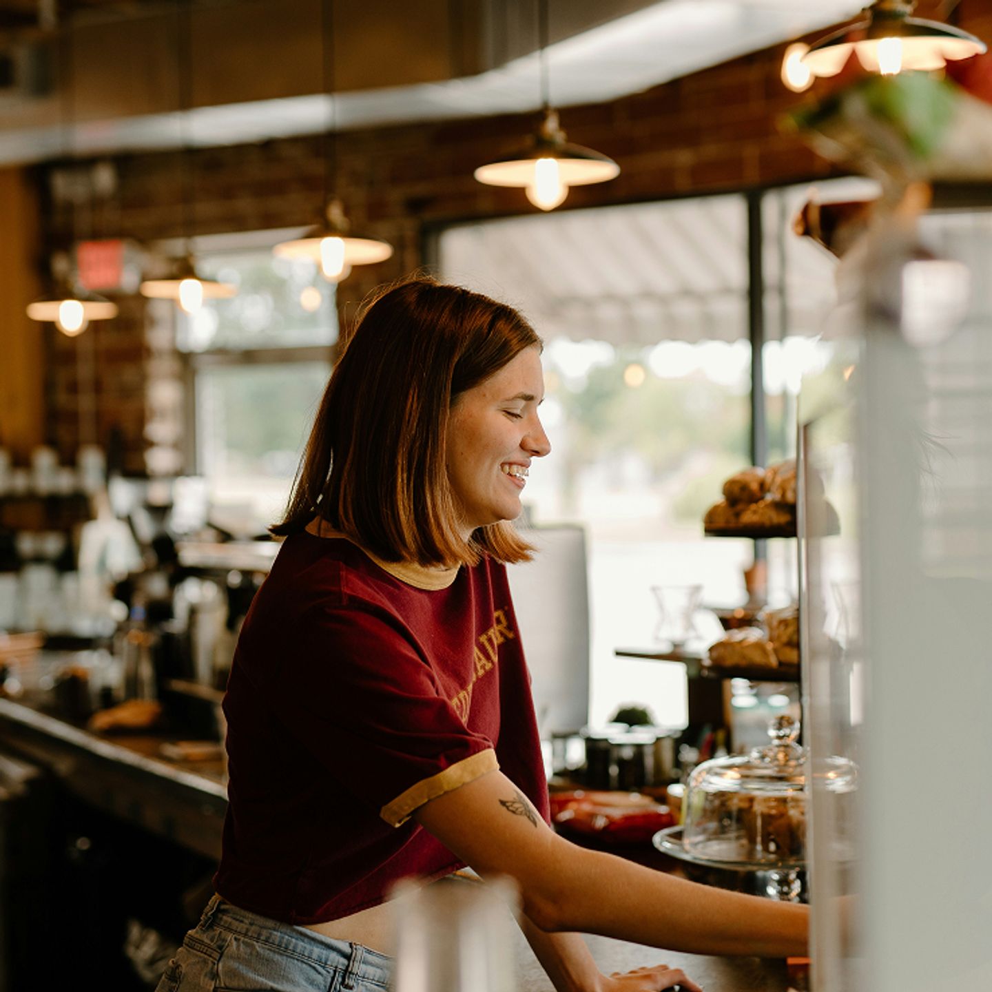 A smiling barista stands behind a cafe counter with pastries in the background.