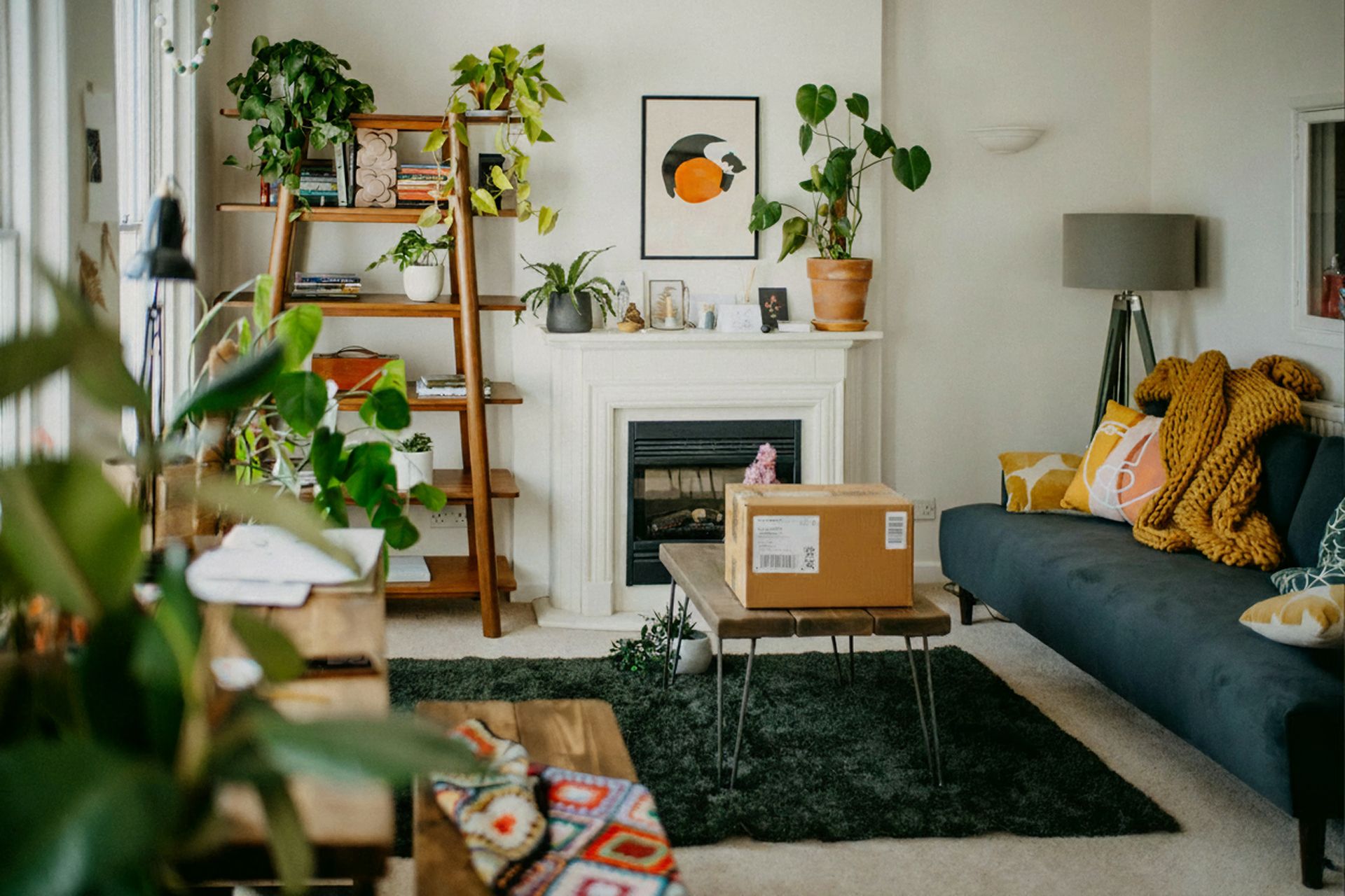 A plant-filled living room with a blue sofa, fireplace, and a package on a coffee table.