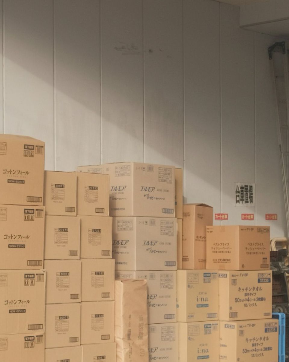 Stacks of cardboard boxes, many labeled in Japanese, fill a room.