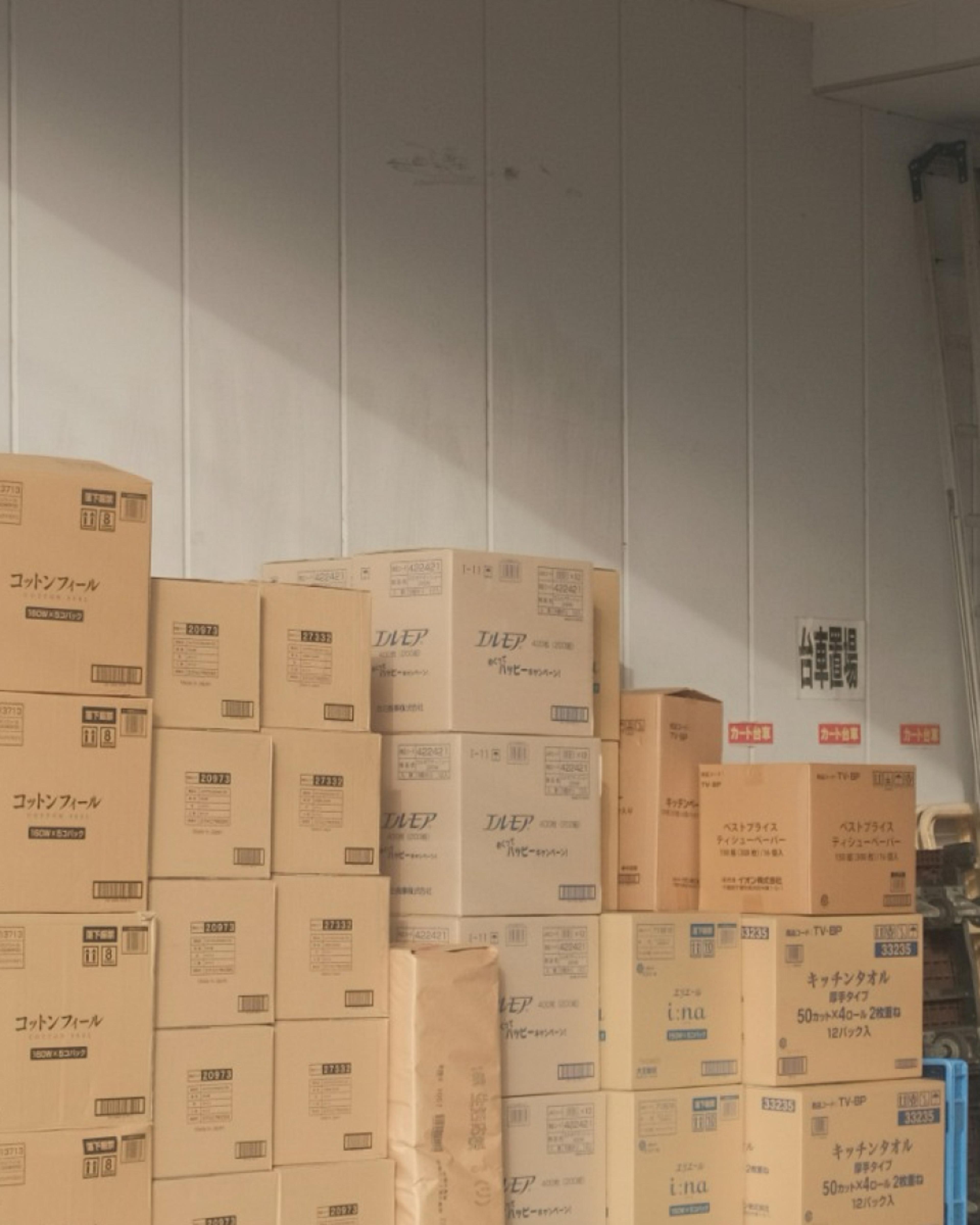 Stacks of cardboard boxes, many labeled in Japanese, fill a room.