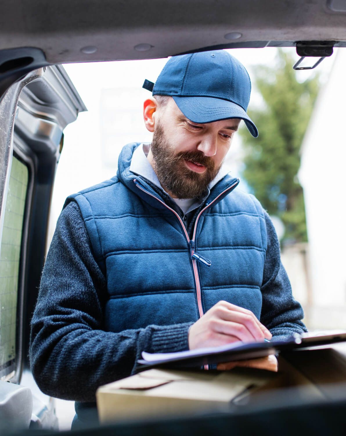 a delivery man is writing on a clipboard while holding a box .
