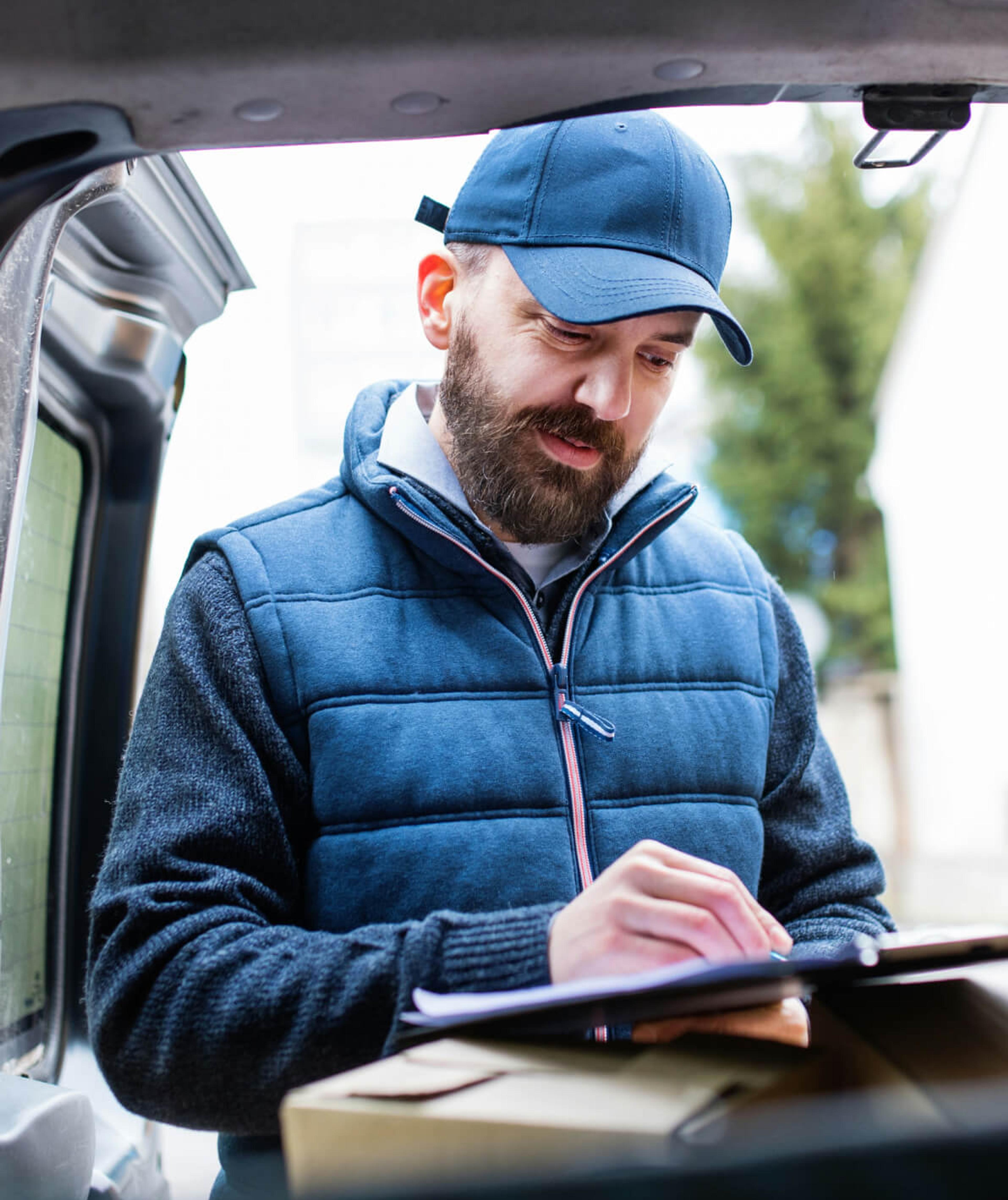 a delivery man is writing on a clipboard while holding a box .