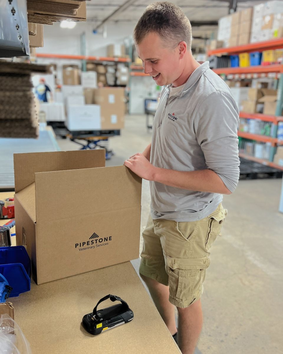 A smiling man packaging a box for Pipestone Veterinary Services in a warehouse.