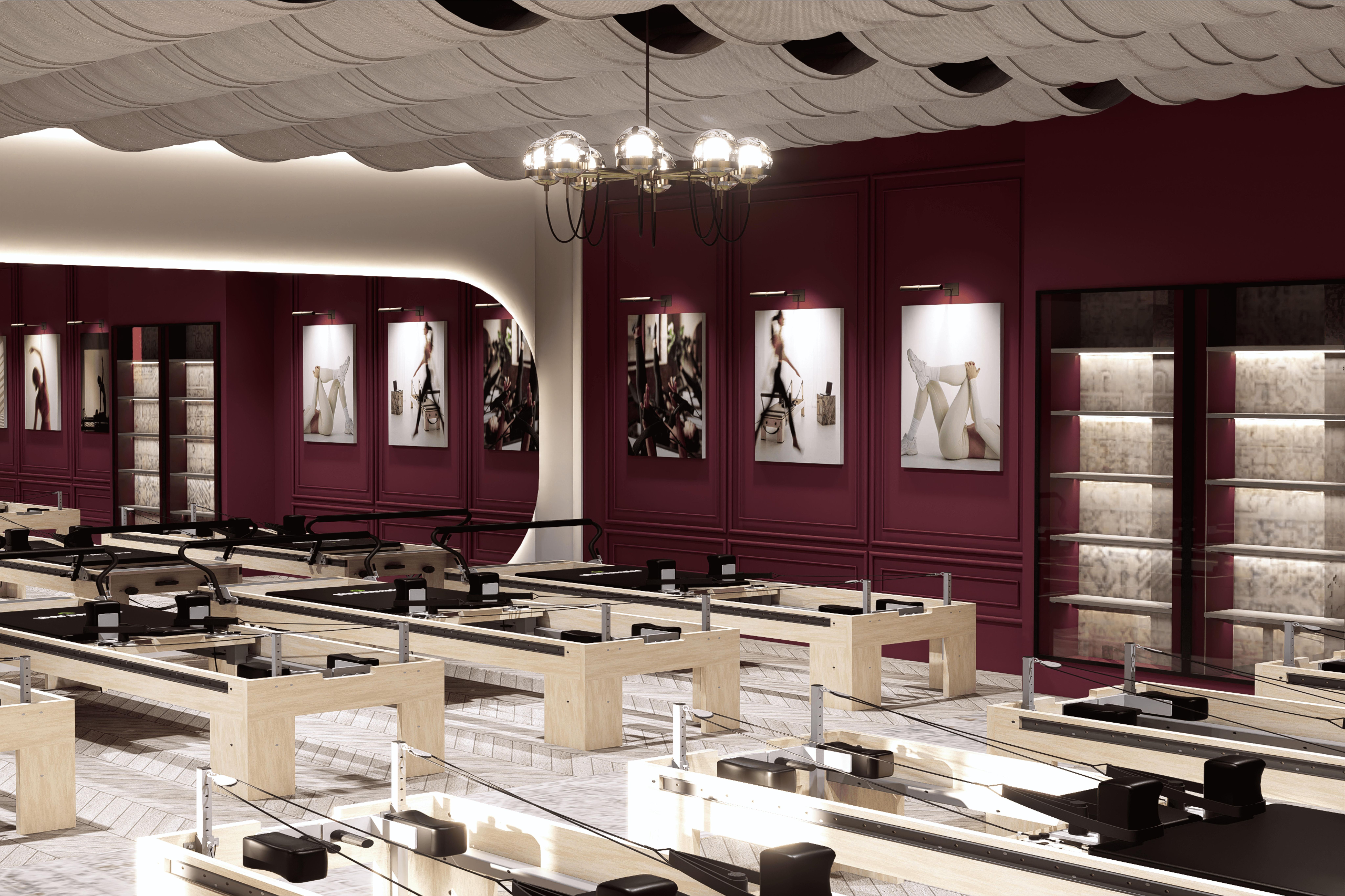 Pilates Estudio - Pilates studio with reformers in rows, deep burgundy panelled walls, herringbone floors and a sculpted wave ceiling.