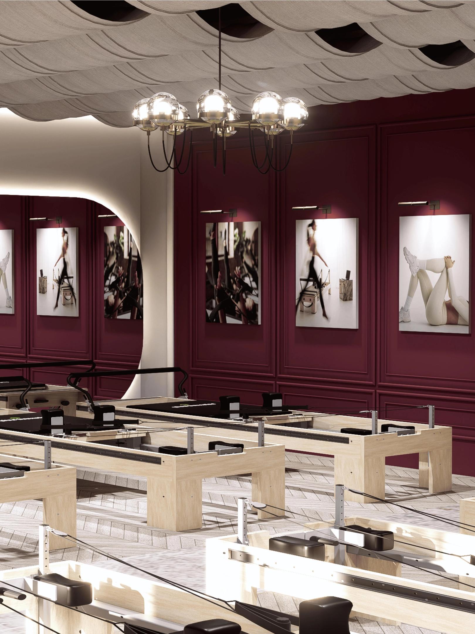 Pilates Estudio - Pilates studio with reformers in rows, deep burgundy panelled walls, herringbone floors and a sculpted wave ceiling.