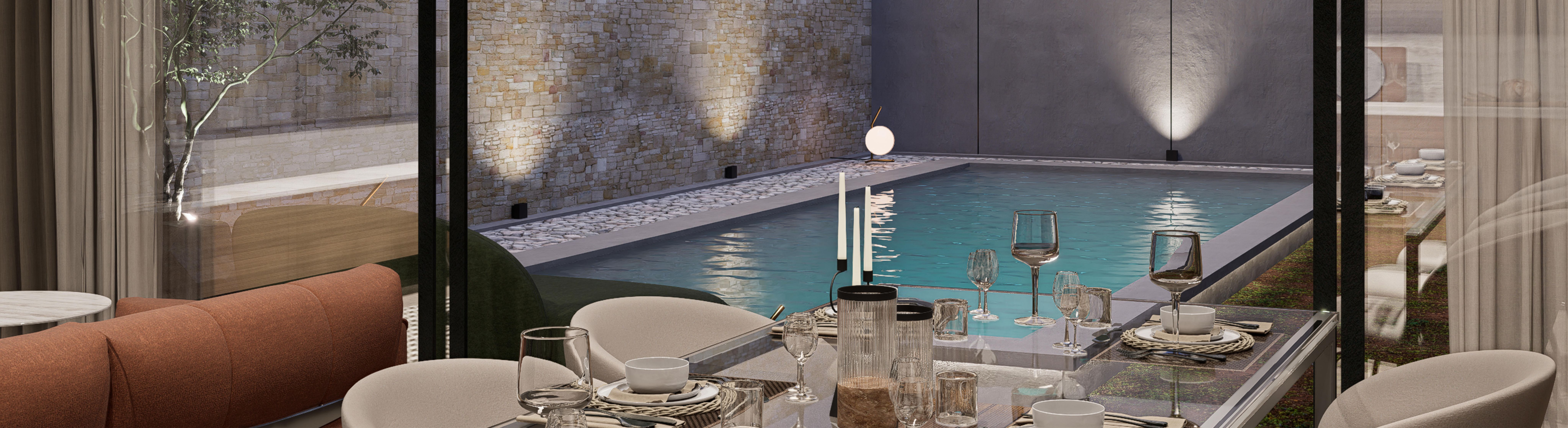Evening view from a set dining table through full-height glass to a lit courtyard pool and stone wall.