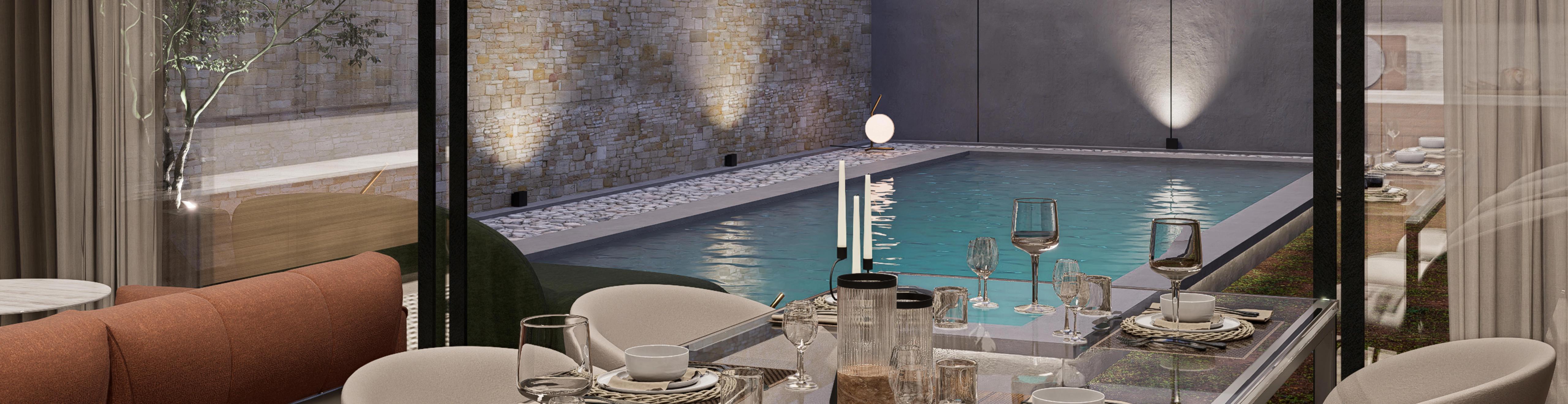 Evening view from a set dining table through full-height glass to a lit courtyard pool and stone wall.