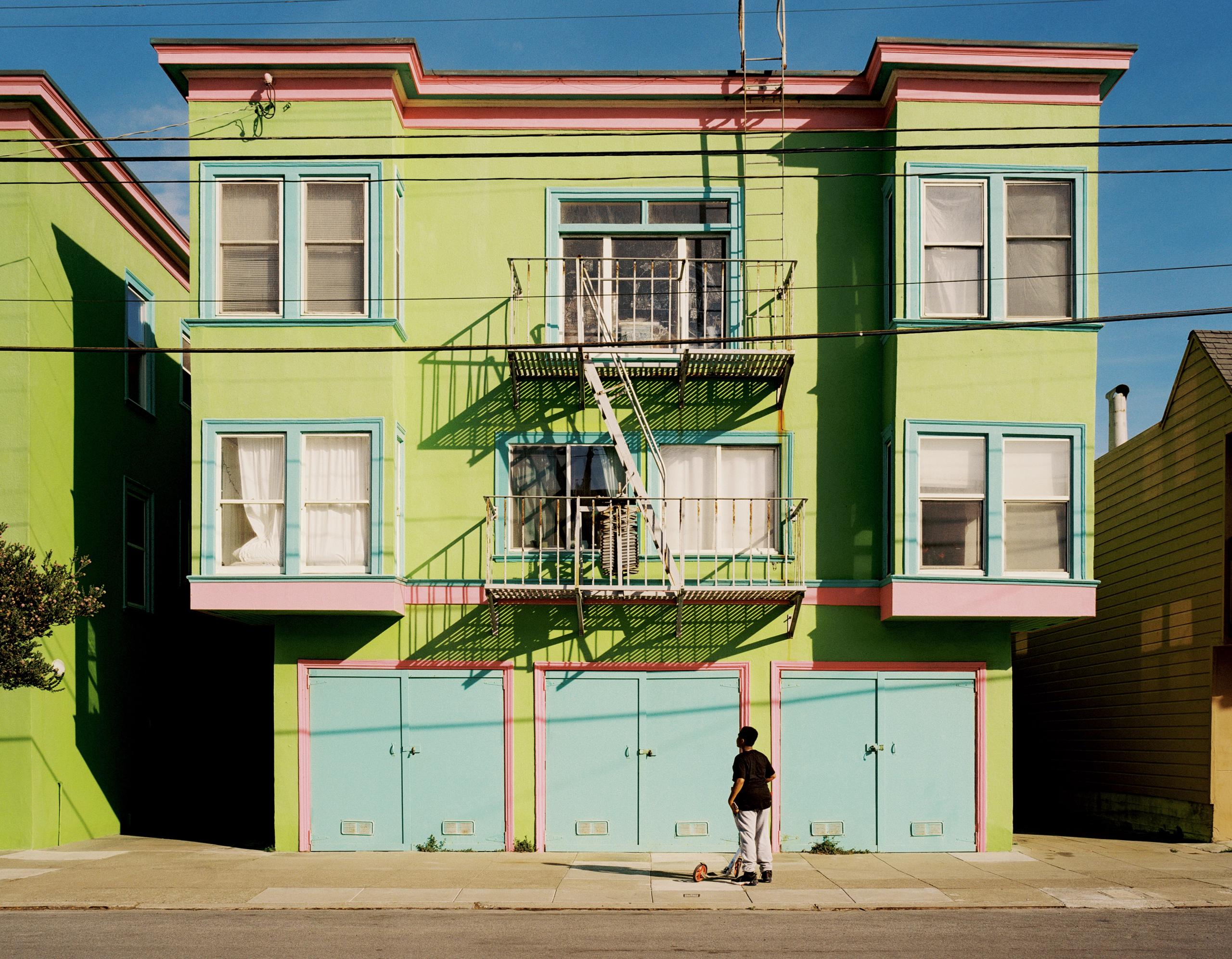 A pastel green San Francisco house with fire escapes and garage doors, a lone passerby below