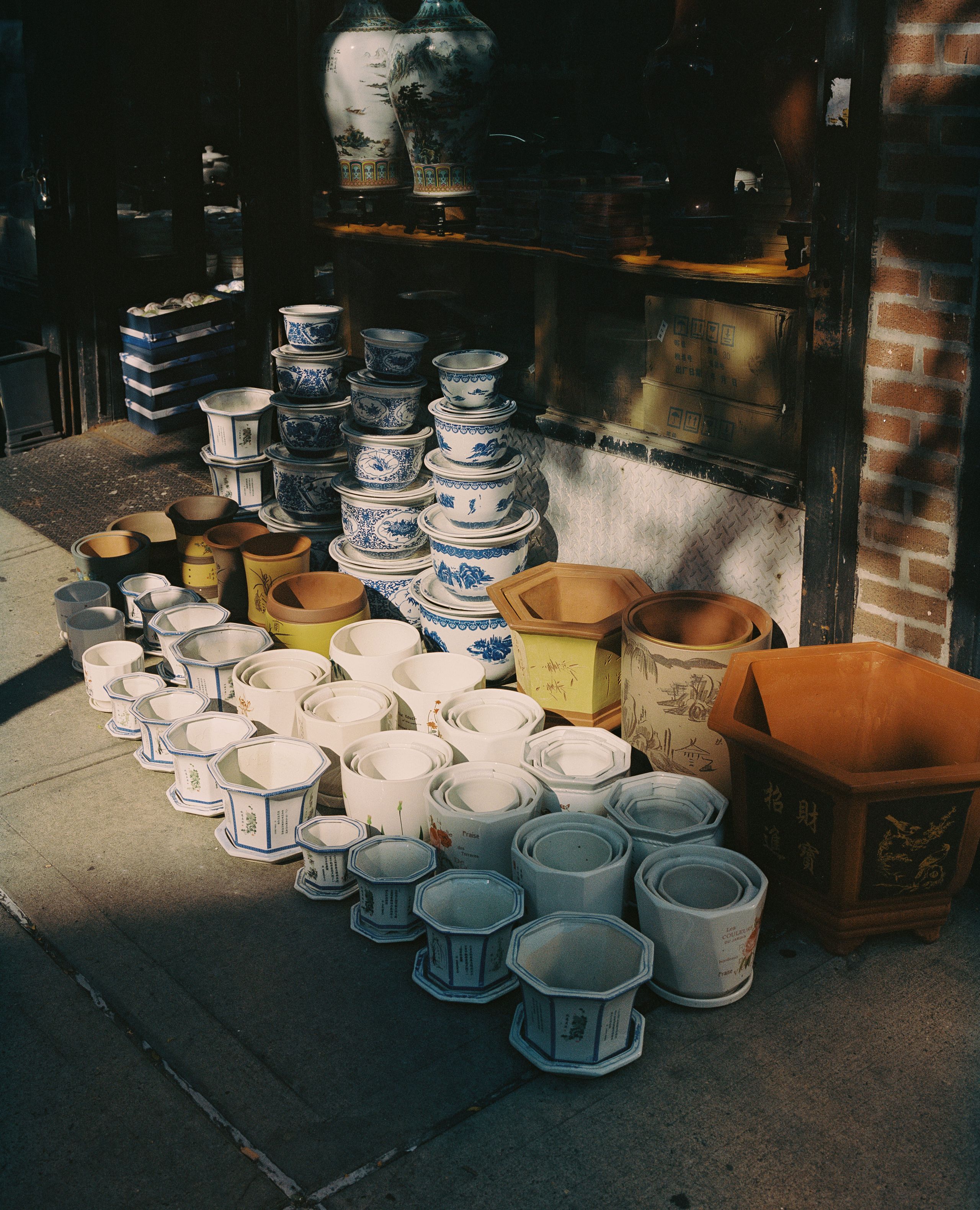 Ceramic pots and bowls set out on a sunlit sidewalk in front of a Chinatown shop