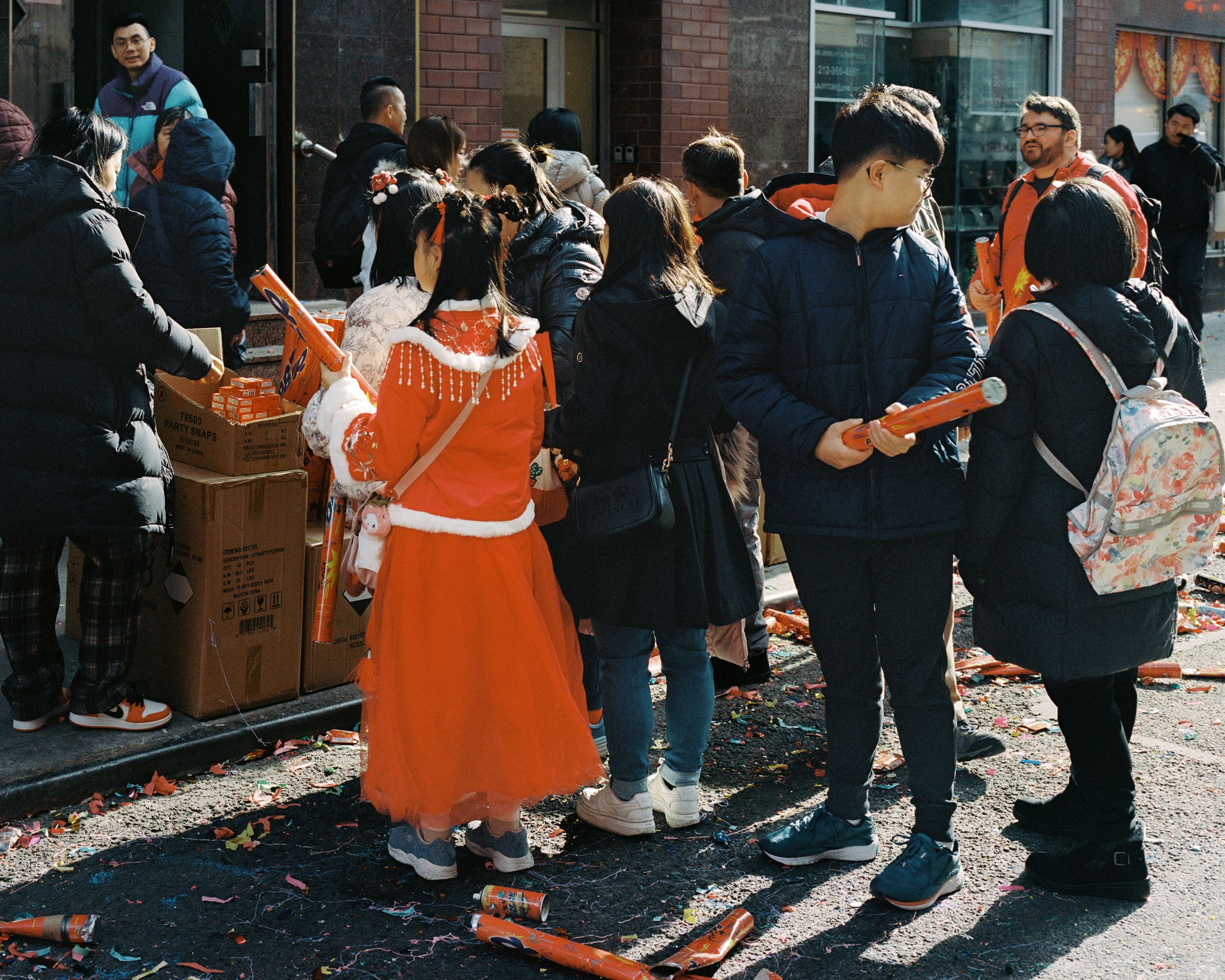 Girl in an orange traditional dress among onlookers on a confetti-covered street