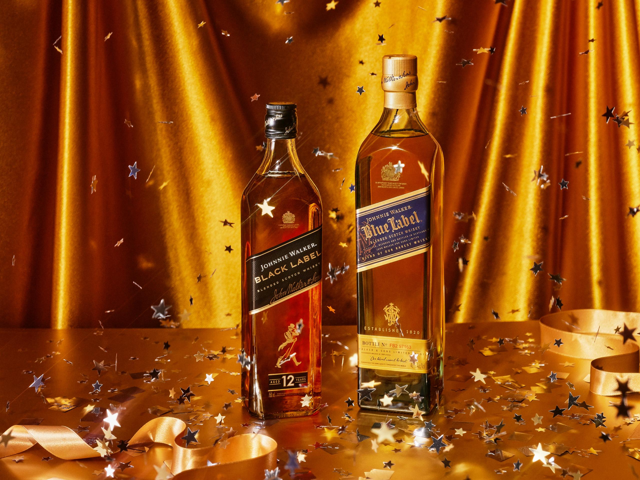 Johnnie Walker Black Label and Blue Label bottles side by side as gold confetti falls against gold satin