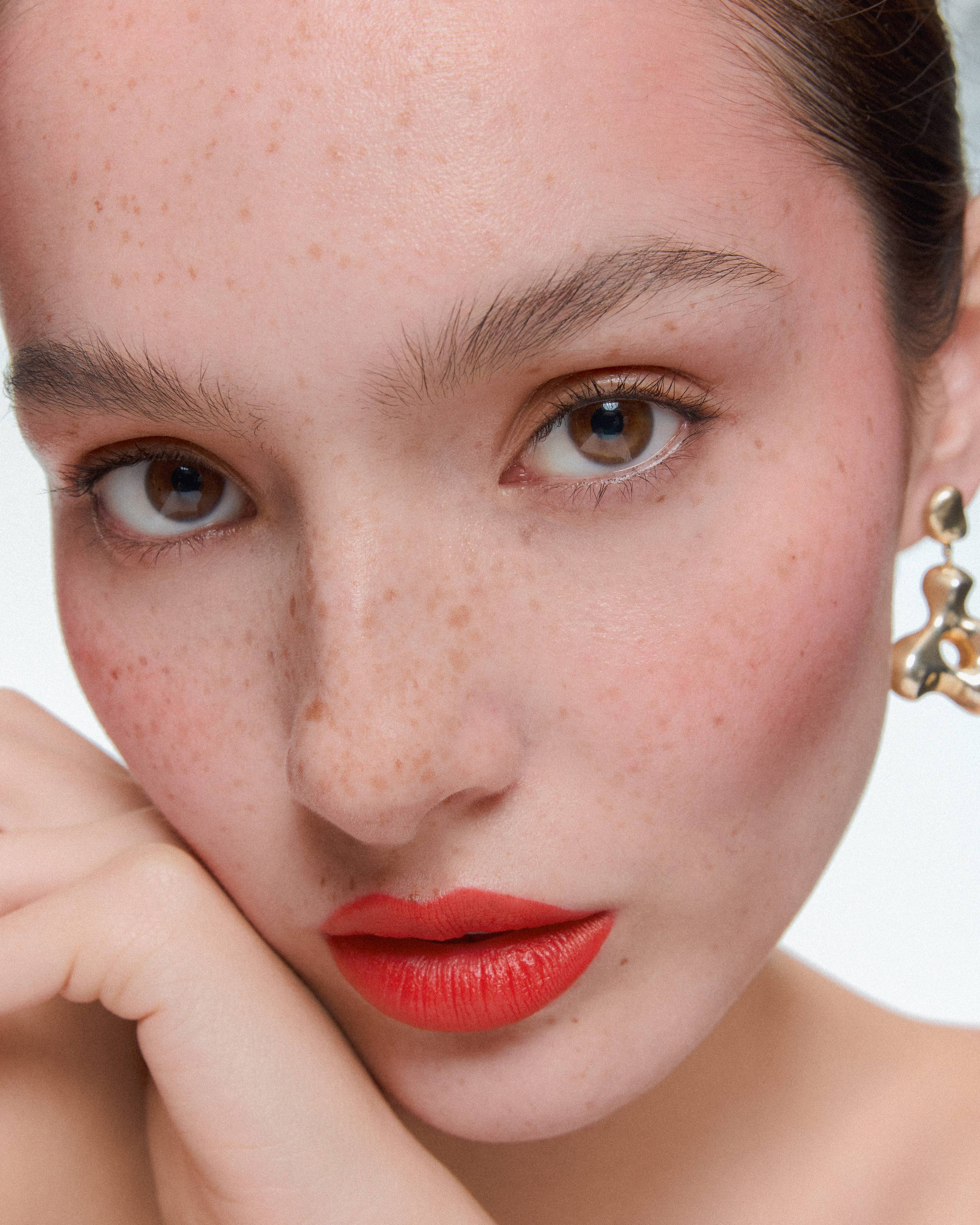 Close-up of model Siobhan wearing sculptural AGMES earrings, with red lips, freckles, and dewy skin in a clean beauty look.