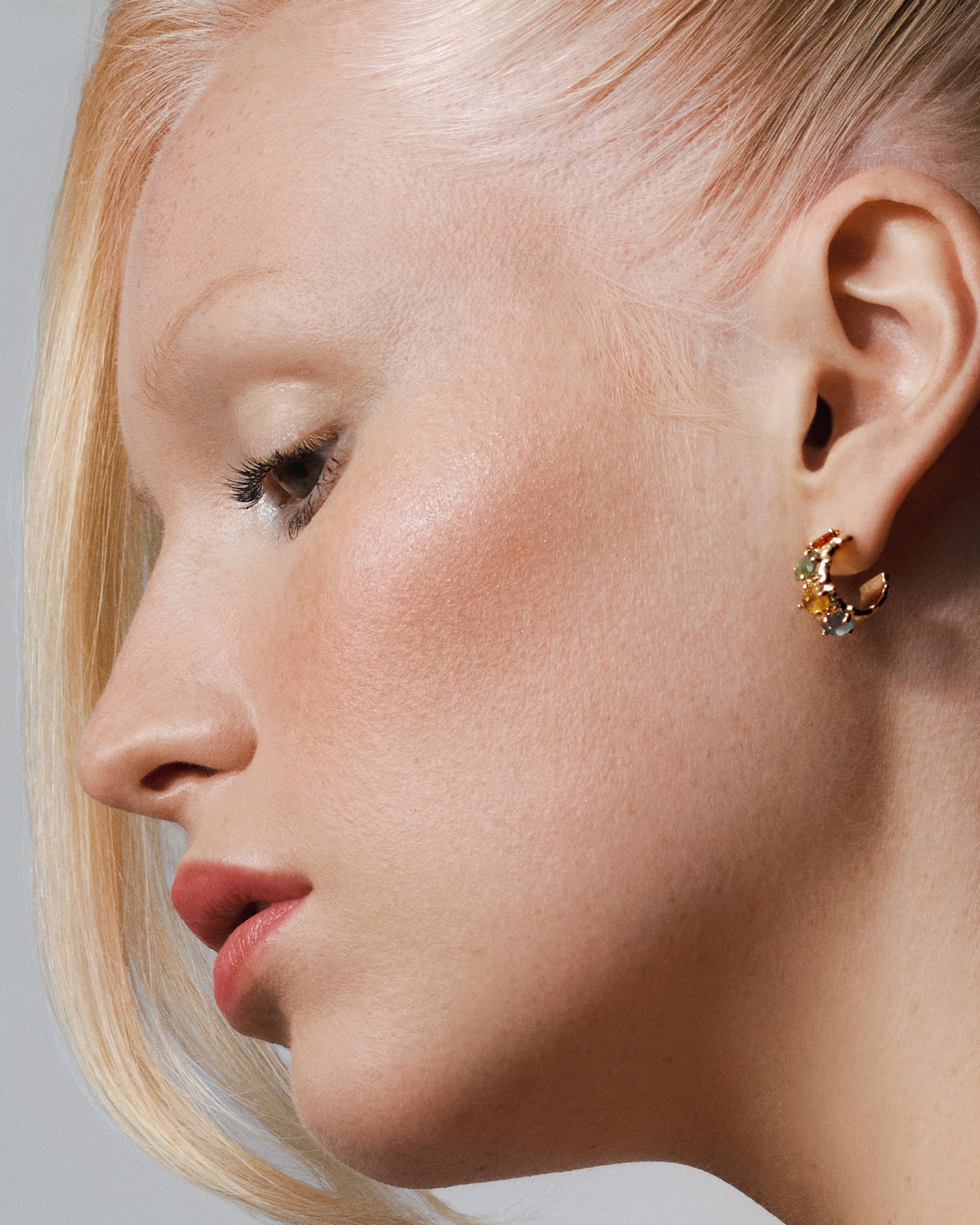 Profile of a platinum-blonde model with luminous skin, soft rose lips and a gold cluster earring