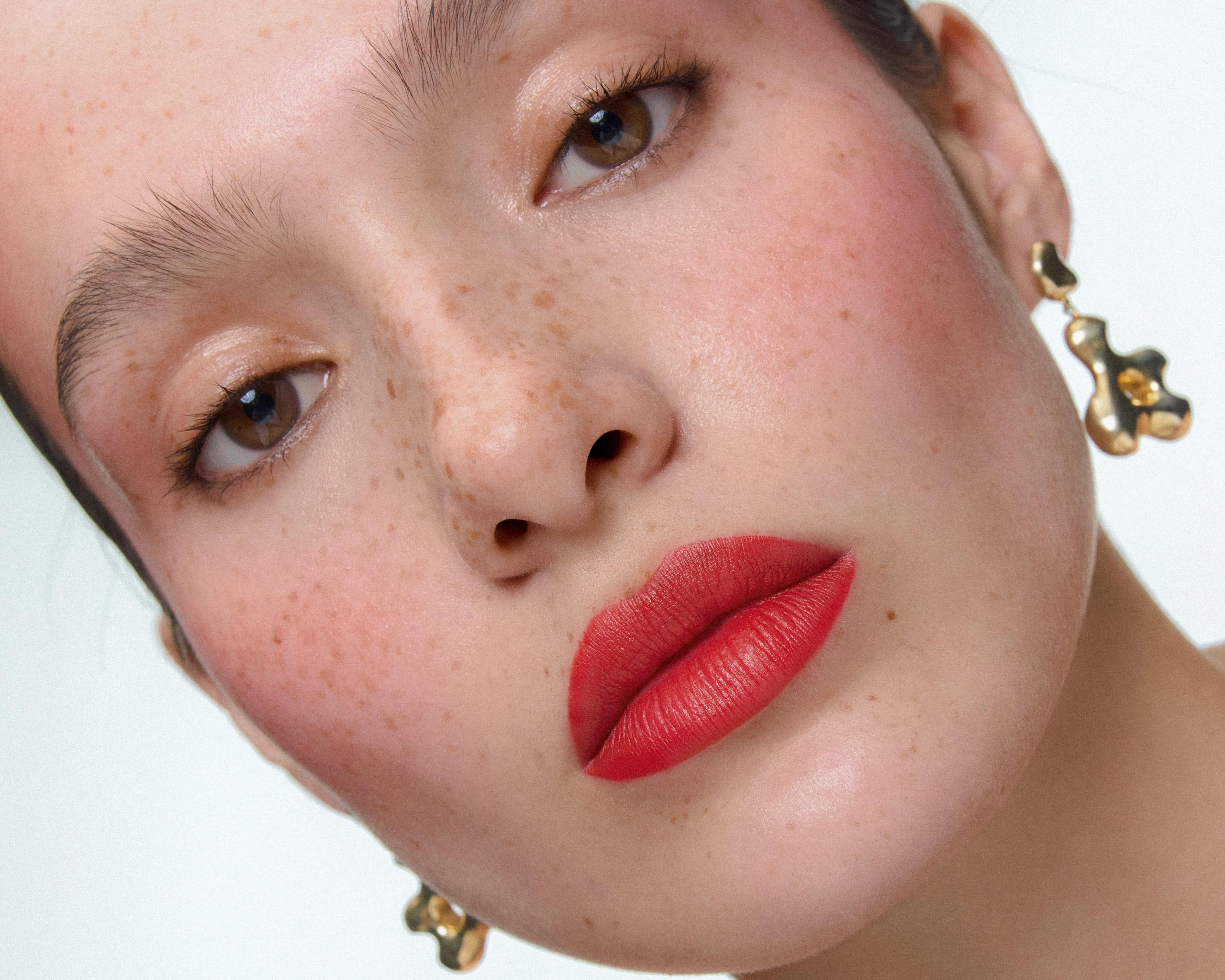 Tilted close-up of Siobhan with freckles, red lips and a gold AGMES earring, her face filling the frame