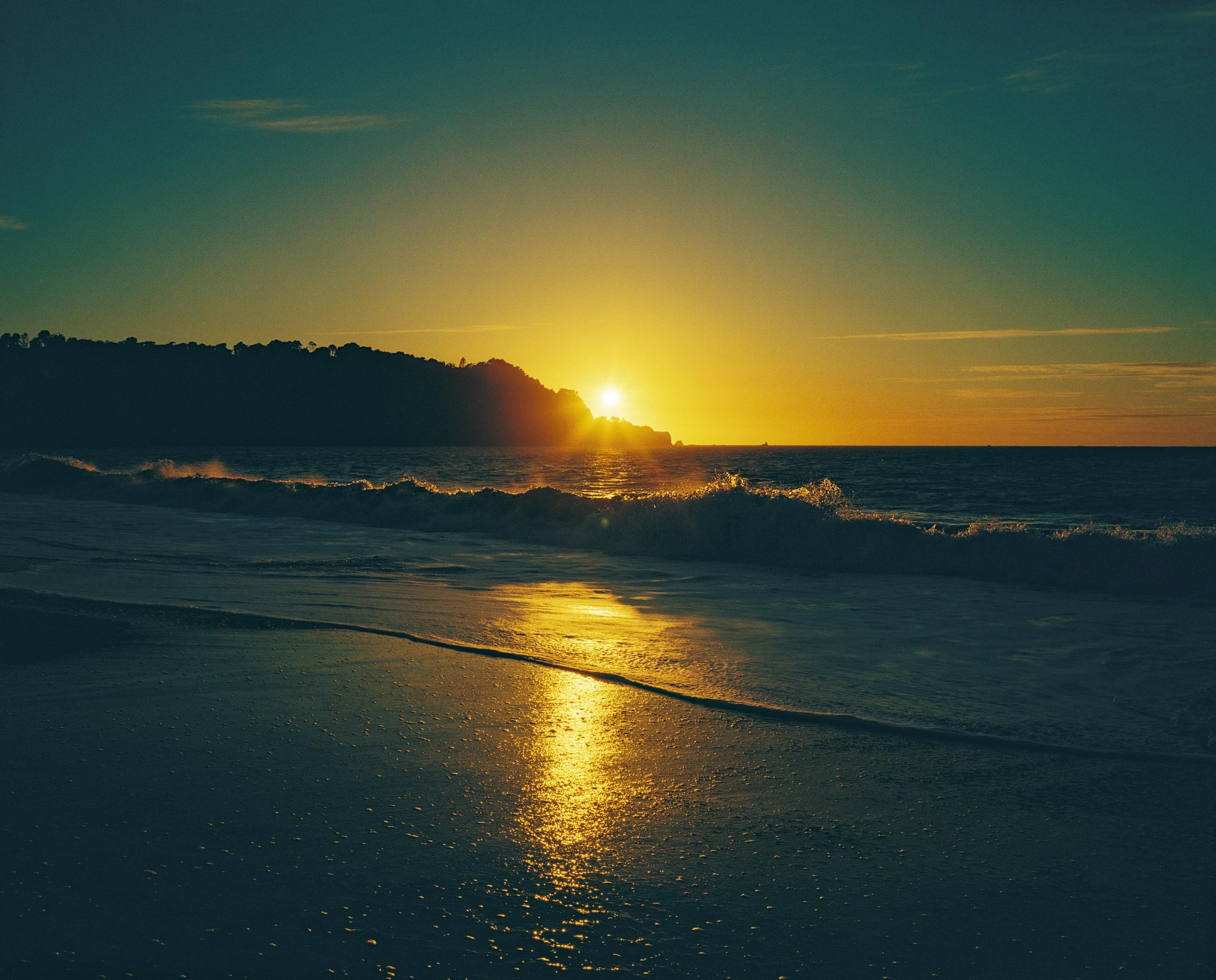 The sun dipping behind the headland, its reflection running across wet sand and surf