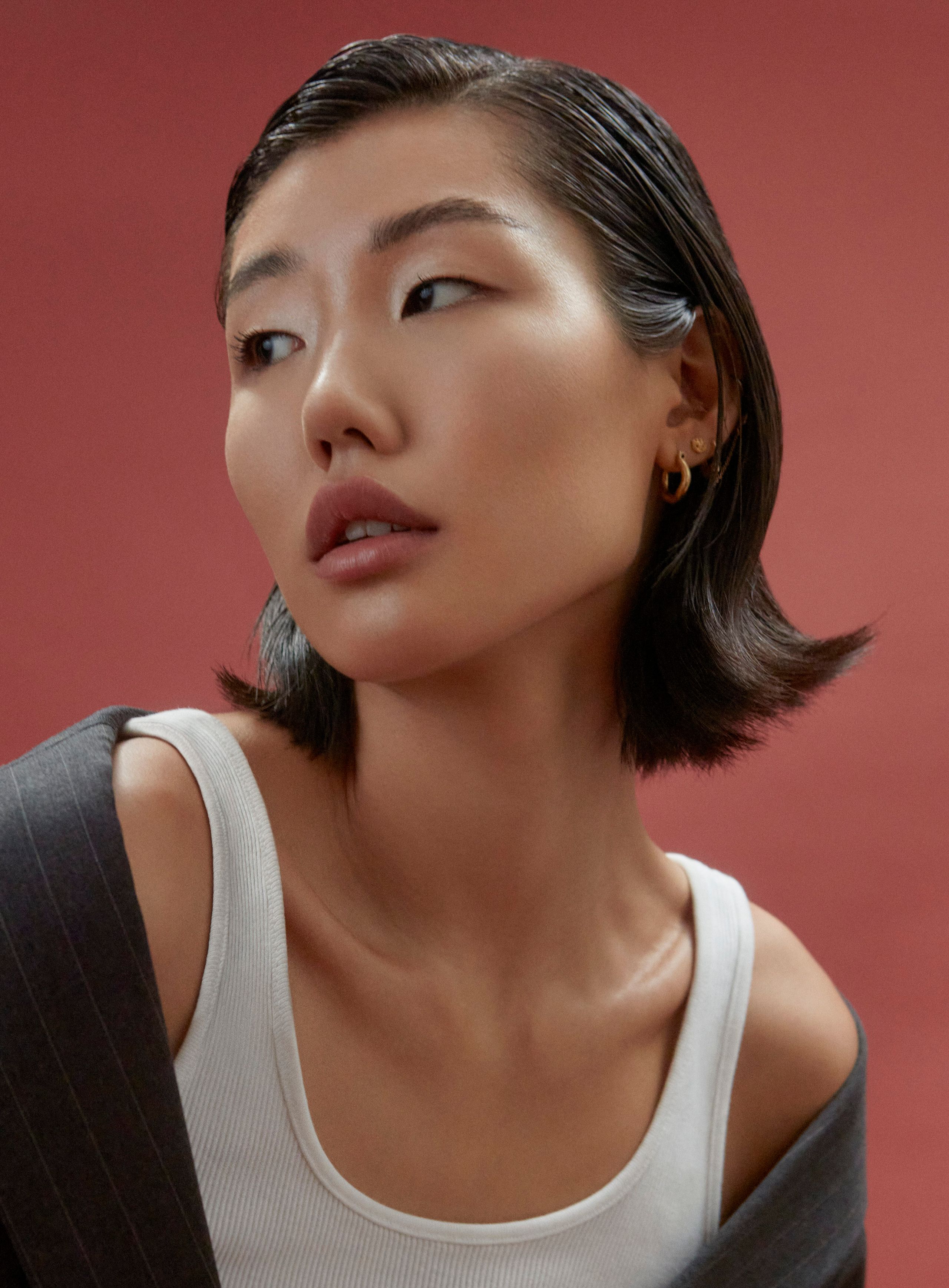 Close-up of Jeannie Jay Park with a wet-look bob and small gold hoops, white tank, gazing past the camera