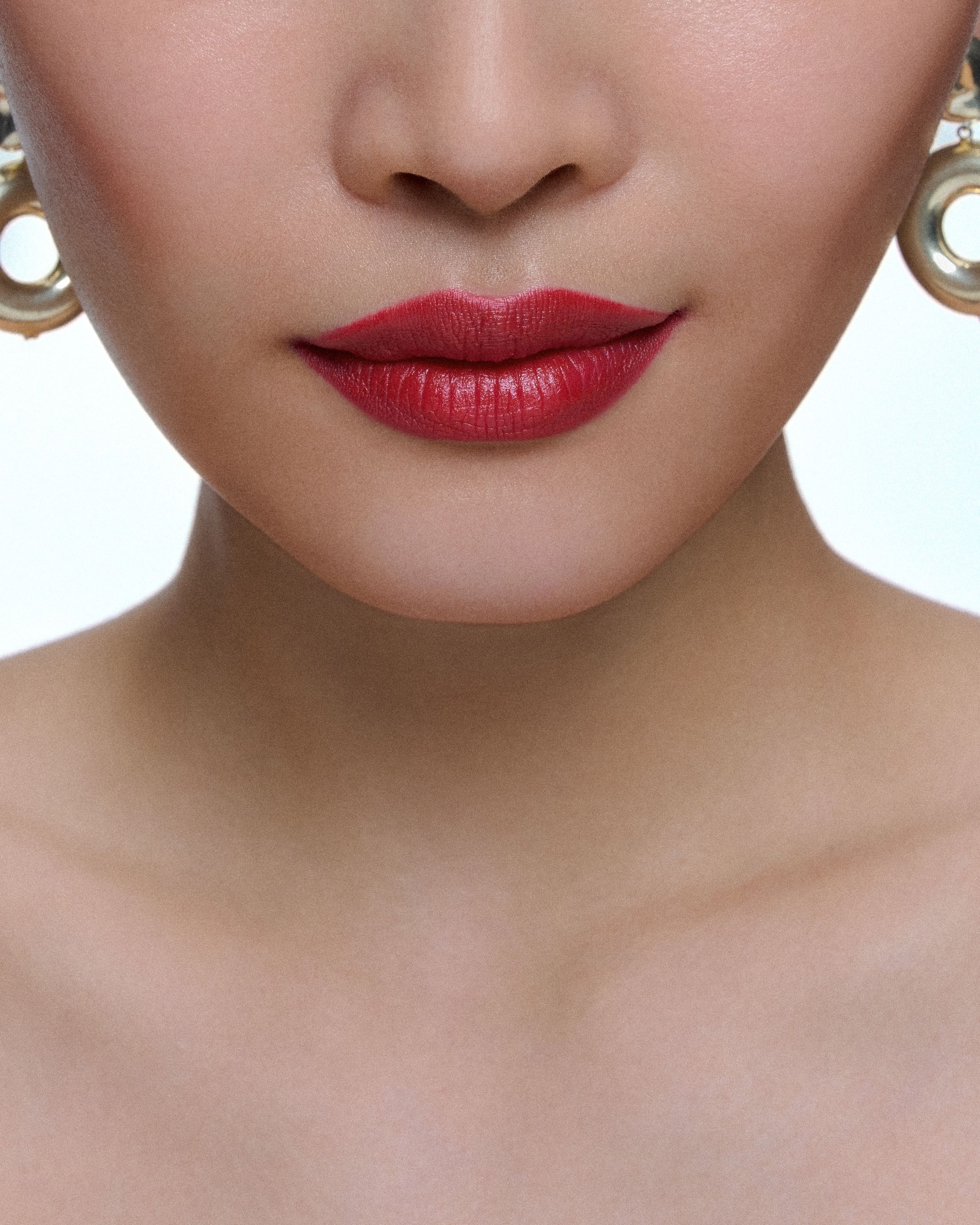 Close-up of deep berry-red lips and bare collarbones, gold AGMES earrings at the edges of the frame