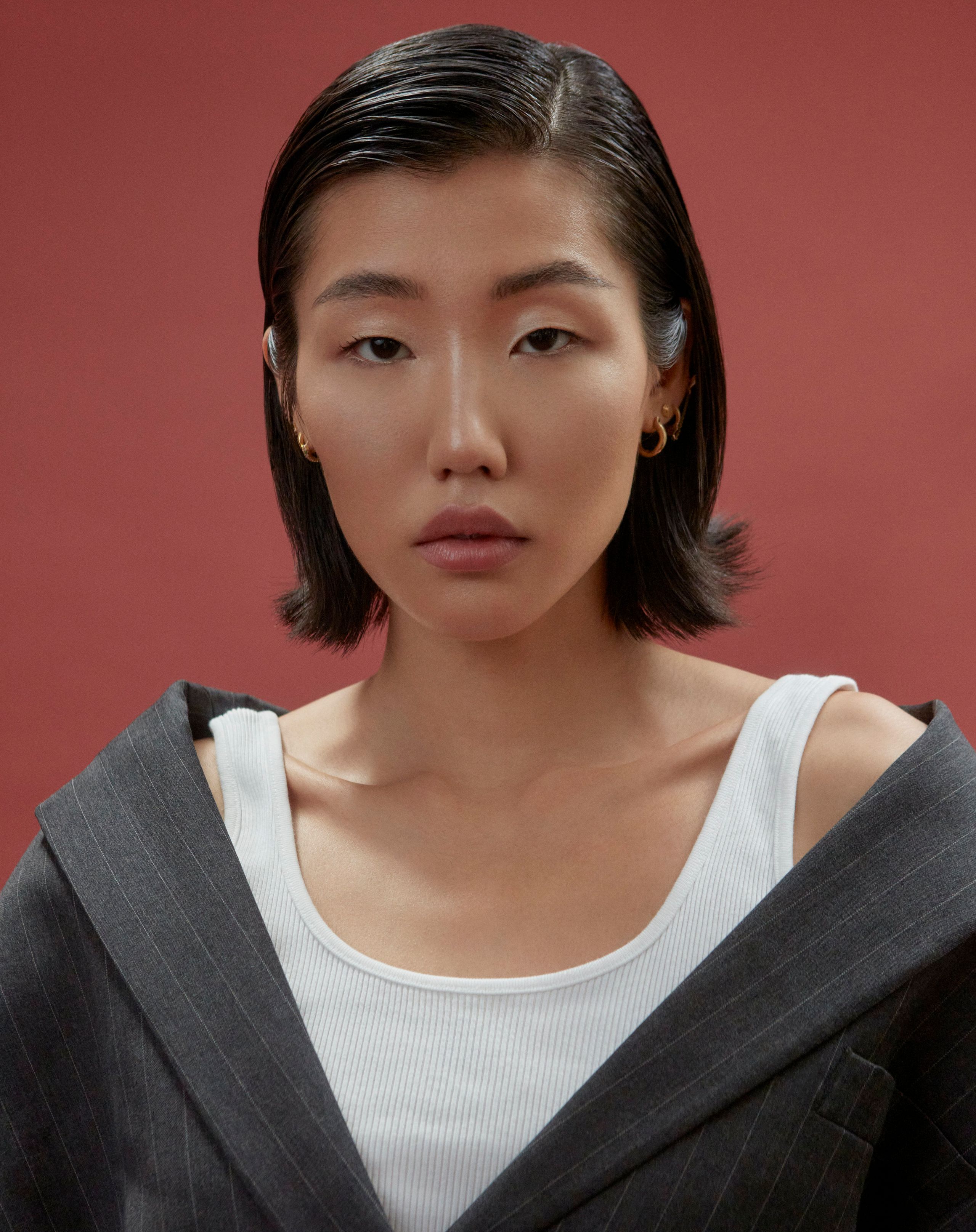 Close-up of Jeannie Jay Park with a sleek bob, white ribbed tank and a blazer slipping off her shoulders, rust backdrop