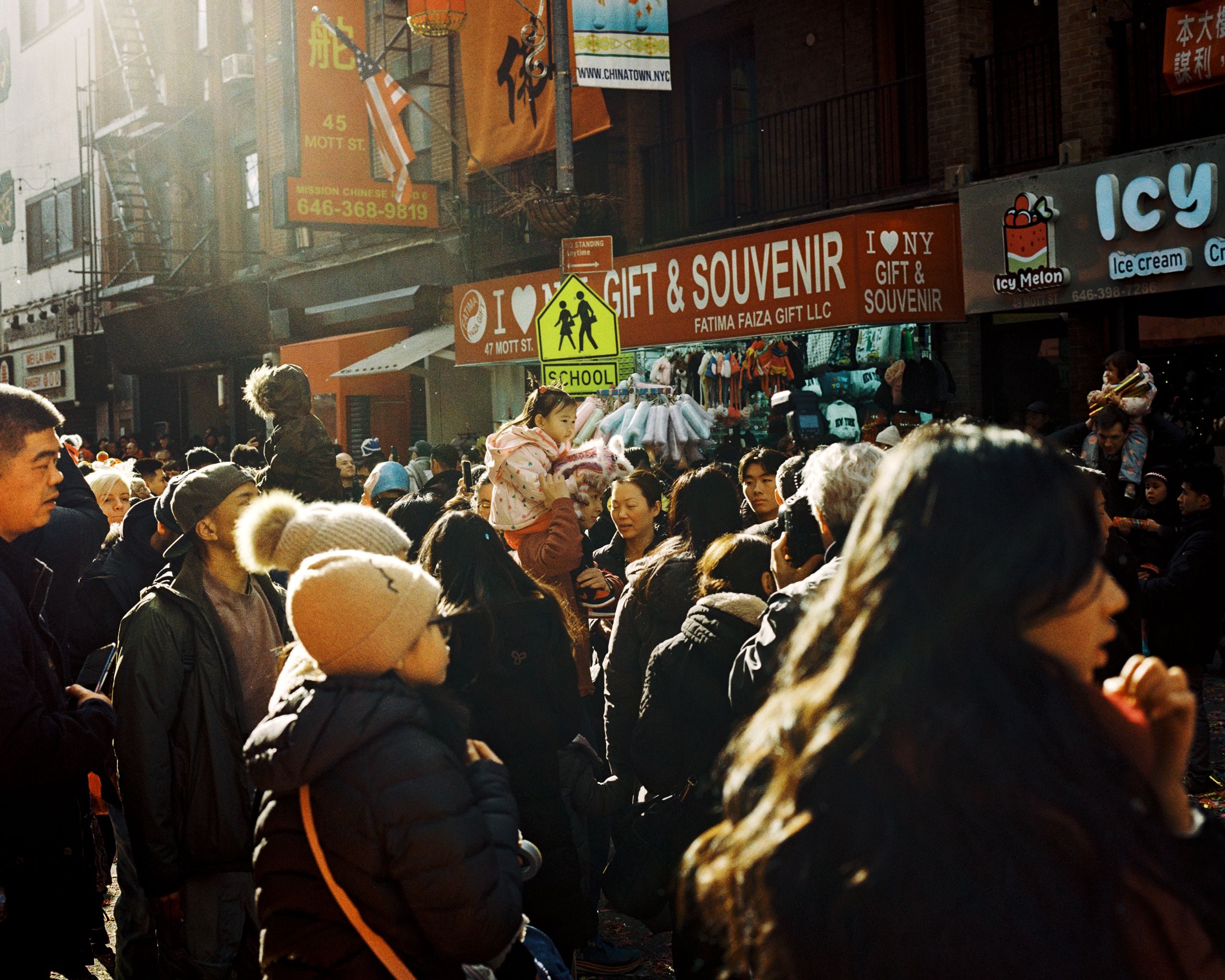 Spectators bundled in winter coats crowding a sunlit Chinatown block of gift shops