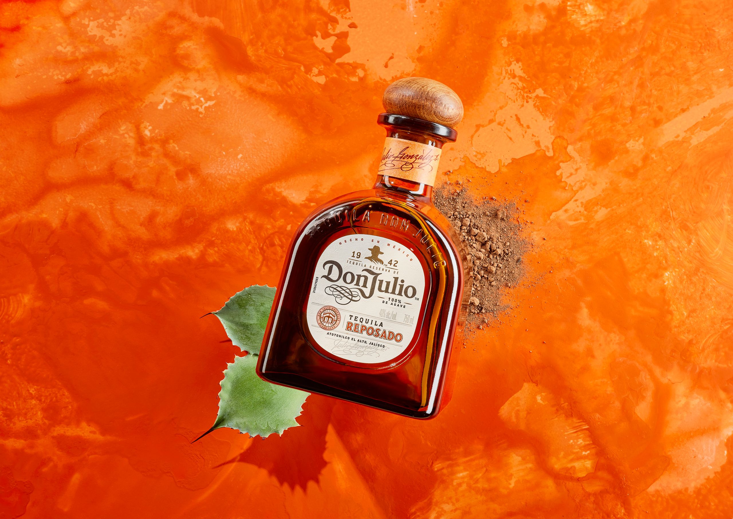 Don Julio tequila bottle on a bright orange painted backdrop beside an agave leaf
